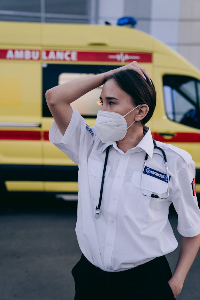 Masked paramedic stands confidently by an ambulance, ready for emergency response.